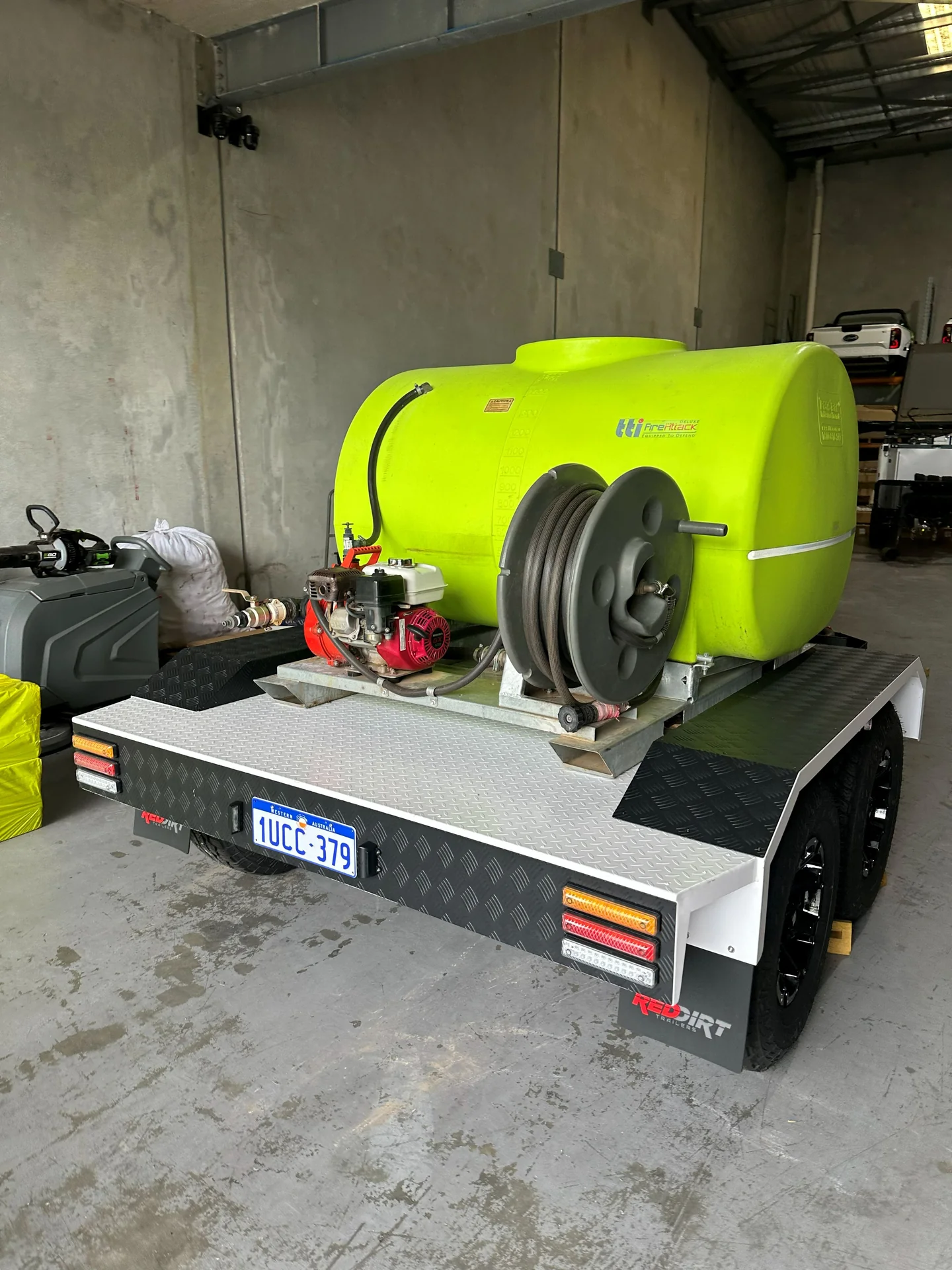 Rear-quarter view of a RedDirt fire fighting trailer showing the TTi tank, petrol-powered pump and manual hose reel